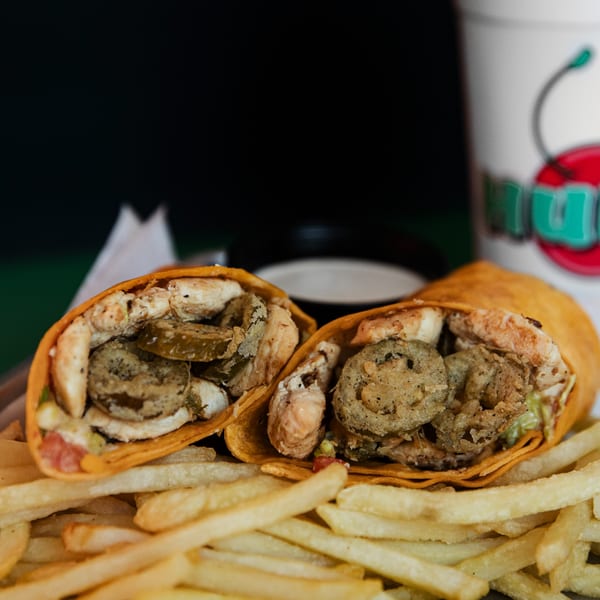 Two Hud's wraps, one with pickles, and a pile of french fries with a drink in the background.