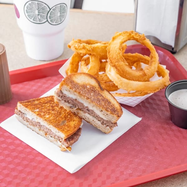 Hud's patty melt with melted cheese and ground beef, served with golden onion rings and dipping sauce.