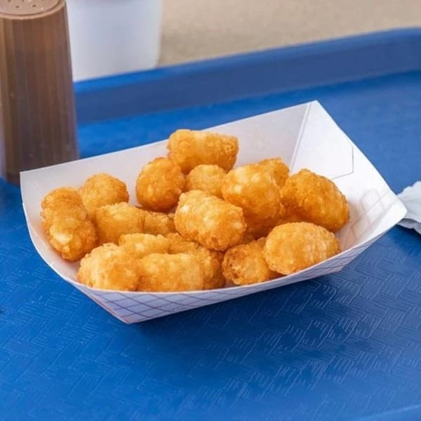 A paper tray filled with golden-brown tater tots sits on a blue textured surface at Hud's.