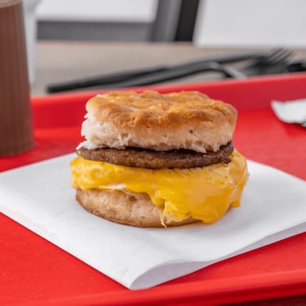 A breakfast sandwich with sausage, egg, and cheese on a biscuit, served on a red tray.