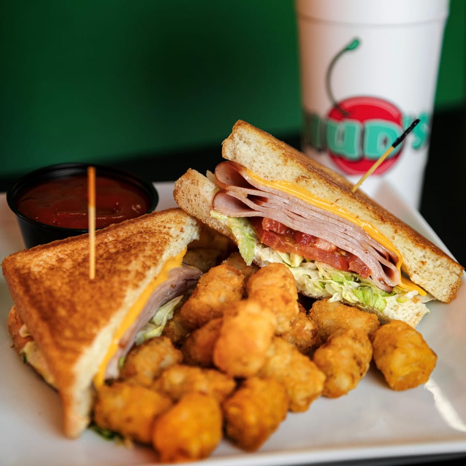 Hud's grilled sandwich with cheese, ham, lettuce, and tomato, served with tater tots and dipping sauce.