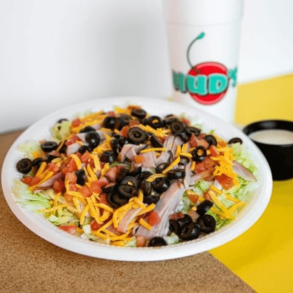 Hud's chef salad with lettuce, ham, cheese, tomatoes, and black olives, with a drink and dressing.