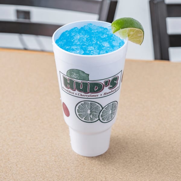 Hud's blue cherrylime drink with crushed ice and a lime wedge on a table.