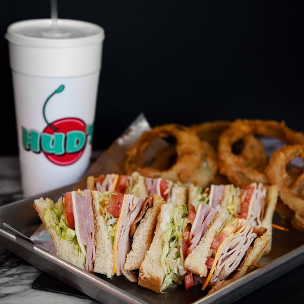 Hud's club sandwiches and onion rings on a tray, with a branded drink cup.
