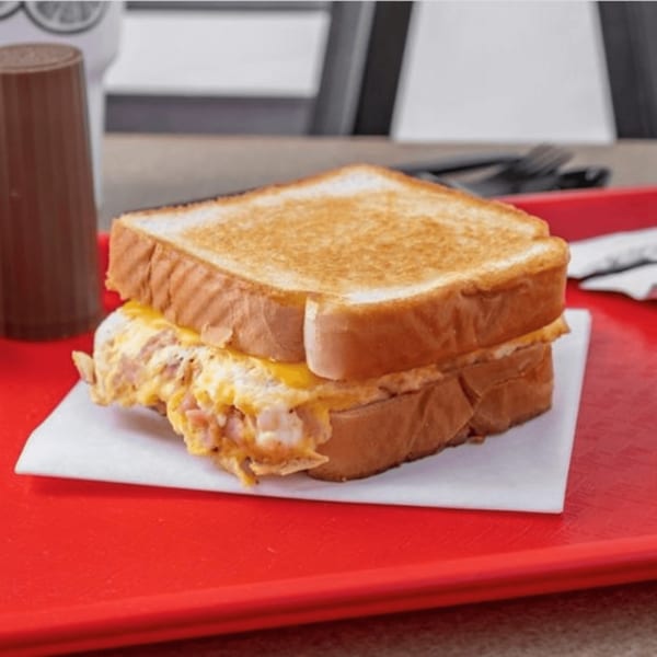 A toasted sandwich with melted cheese and meat on a white napkin, served on a red tray.
