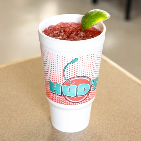 A Hud's branded cup filled with a red crushed ice drink and a lime wedge.