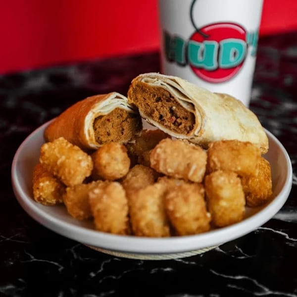A plate of Hud's burritos, one cut open, and tater tots, with a Hud's drink cup in the background.