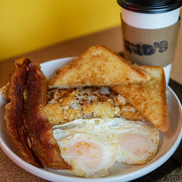 Hud's American breakfast with crispy bacon, fried eggs, hash browns, toast, and coffee.