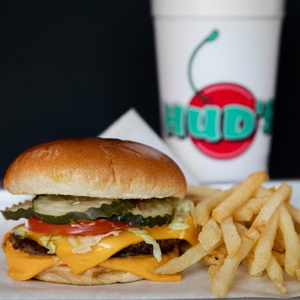 A Hud's double cheeseburger with pickles, tomato, and lettuce, served with fries and a drink.