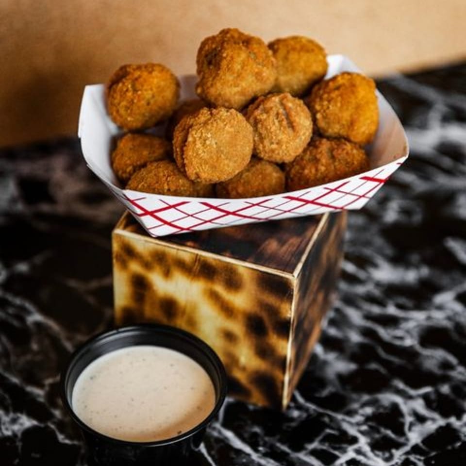 Hud's fried hushpuppies in a paper tray with a side of dipping sauce on a dark marble surface.