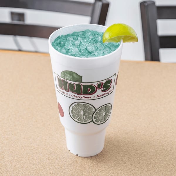 A Hud's cherrylime drink, a blue slushy with a lime wedge, on a table.